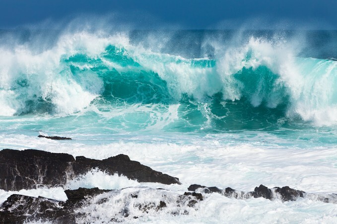 Turquoise rolling wave slamming on the rocks of the coastline